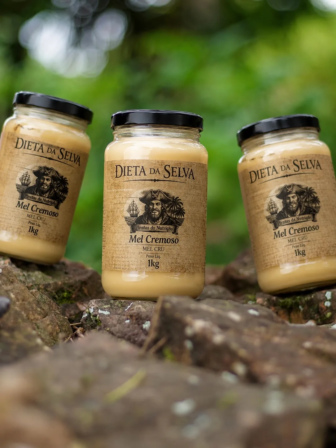 Três potes de Mel Cremoso da Selva sobre pedras, na mata